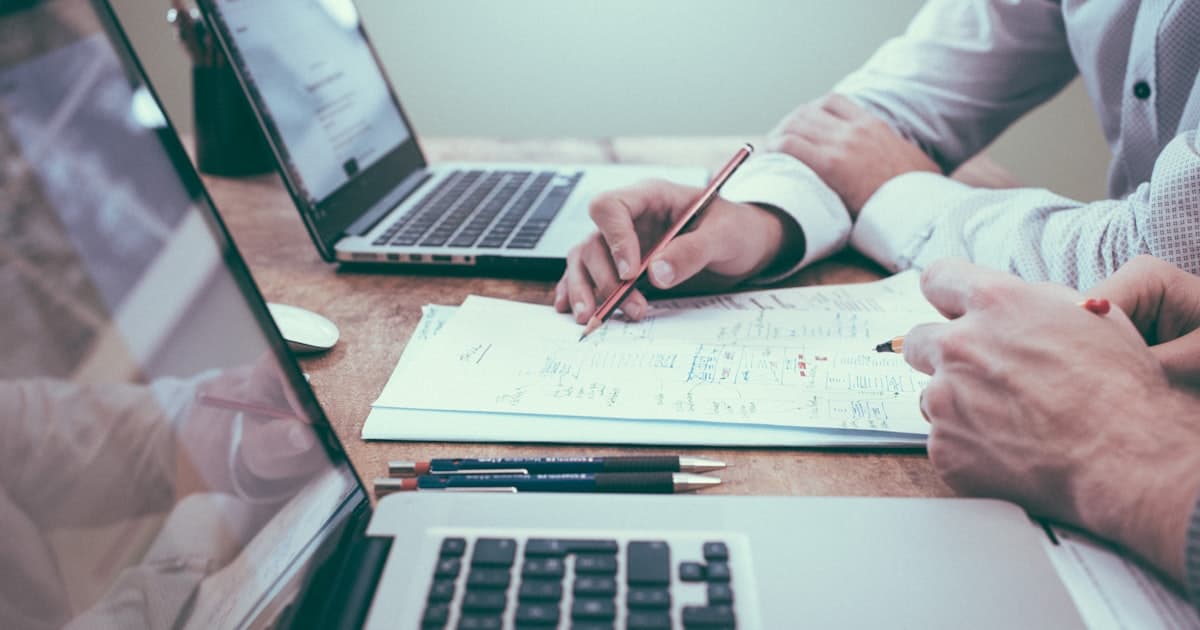 Professional reviewing project documents and planning notes beside a laptop at a desk